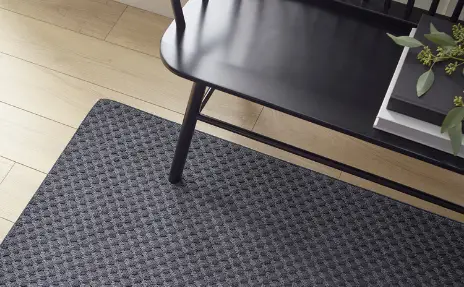 black textured area rug under black colonial bench in entry way with light wood floors